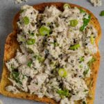 Miso tuna salad on toast on a grey board with tuna and herbs.