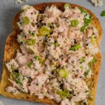 Miso tuna salad on toast on a grey board with tuna and herbs.