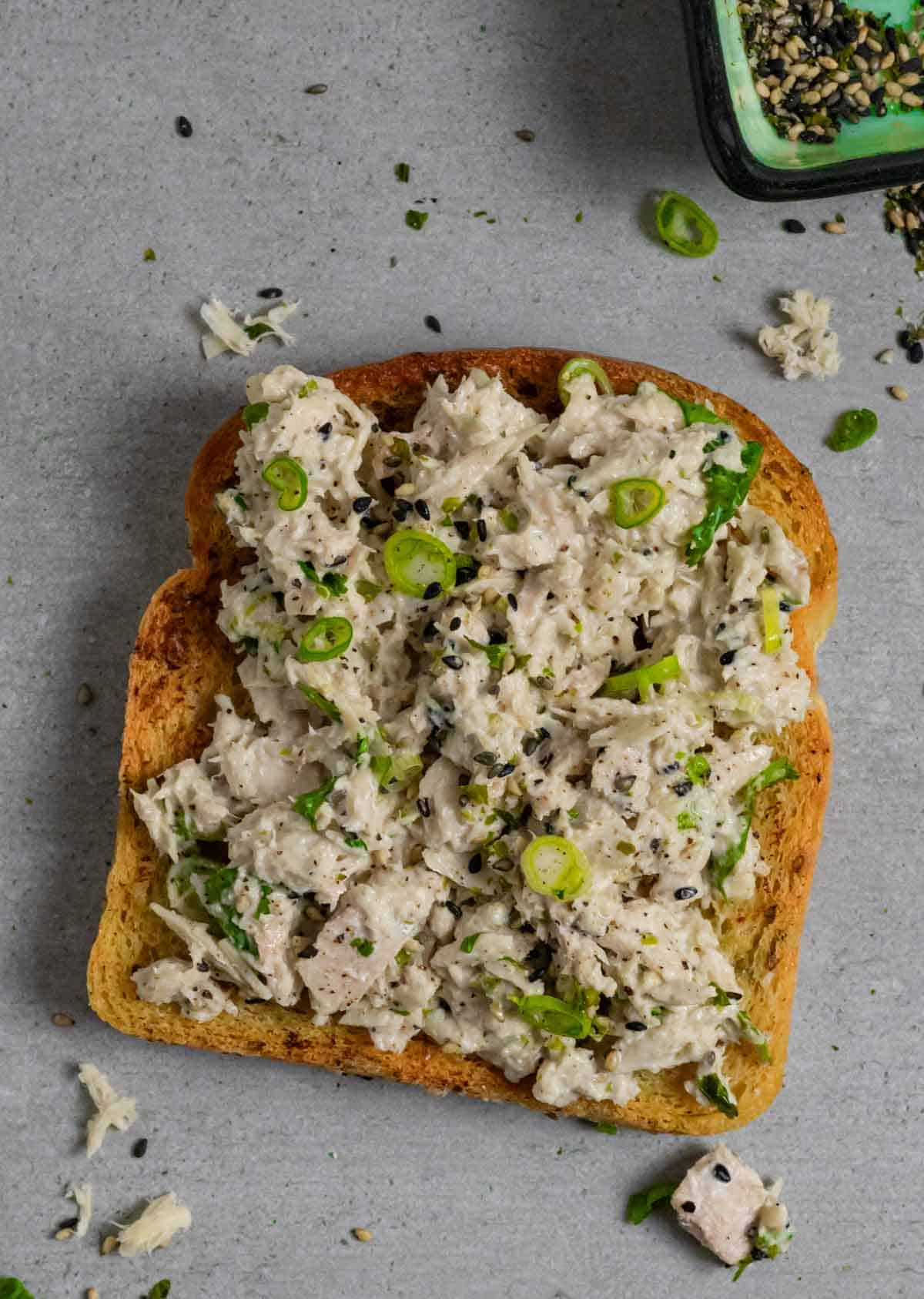 Miso tuna salad open faced on toast with bowl of sesame seeds.