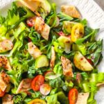 Lebanese fattoush salad on a white plate topped with sumac dressing and crisp tortilla pieces.