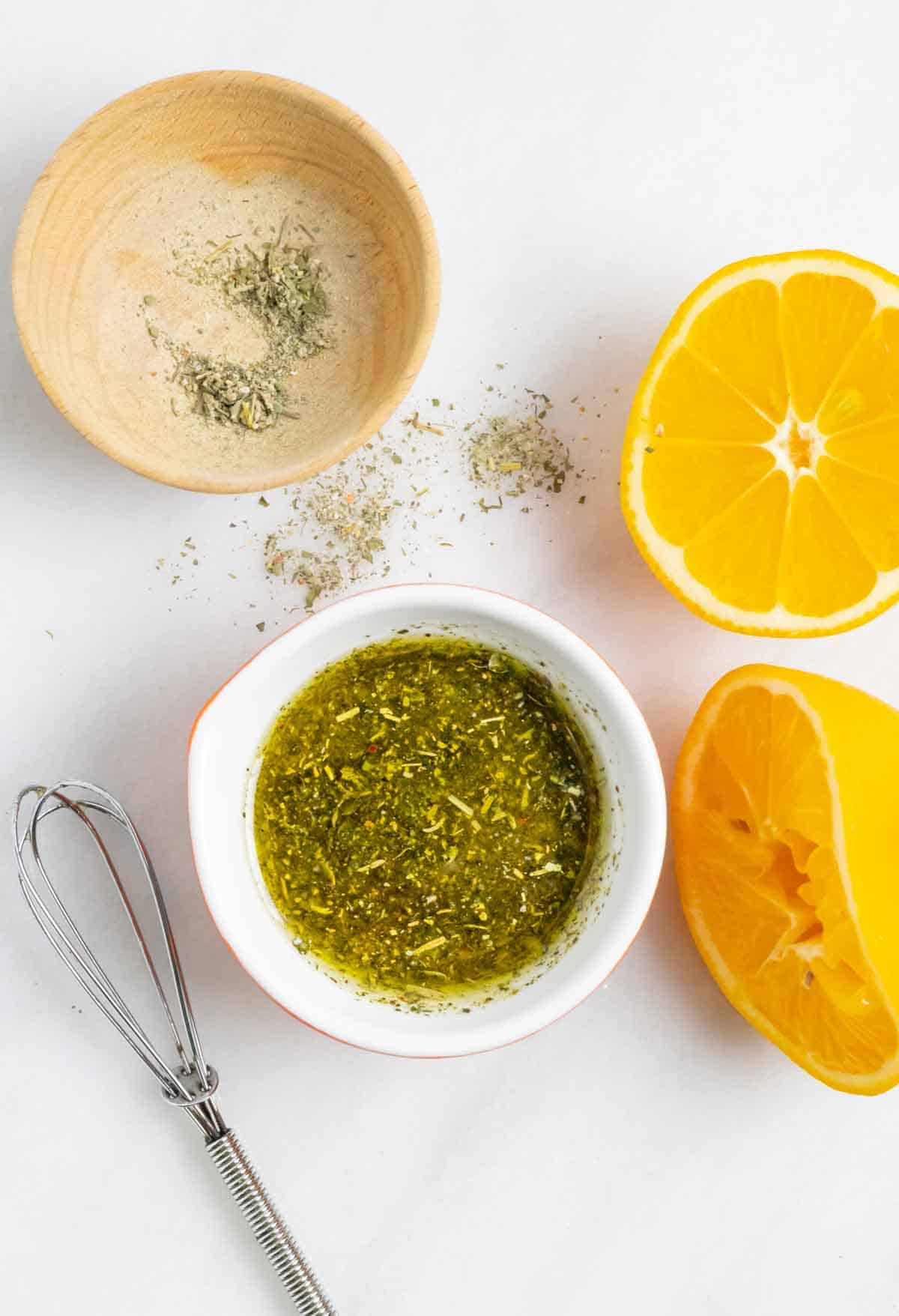 Small wood bowl with herbs, small bowl with herbs and lemon juice mixed, and a cut in half lemon with half of it squeezed.