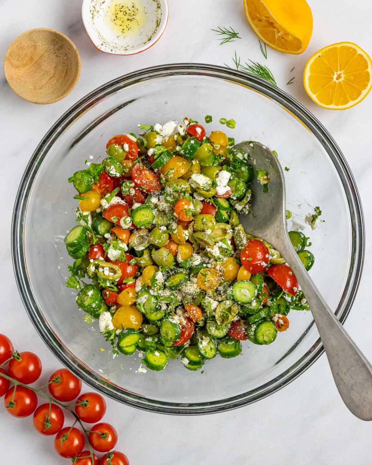 Cucumber tomato mediteranean salad in a clear bowl mixed with dressing and feta.