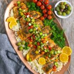 Seven pieces of Mediterranean seasoned steelhead trout on a bed of cauliflower rice on a copper tray garnished with tomato cucumber salad.