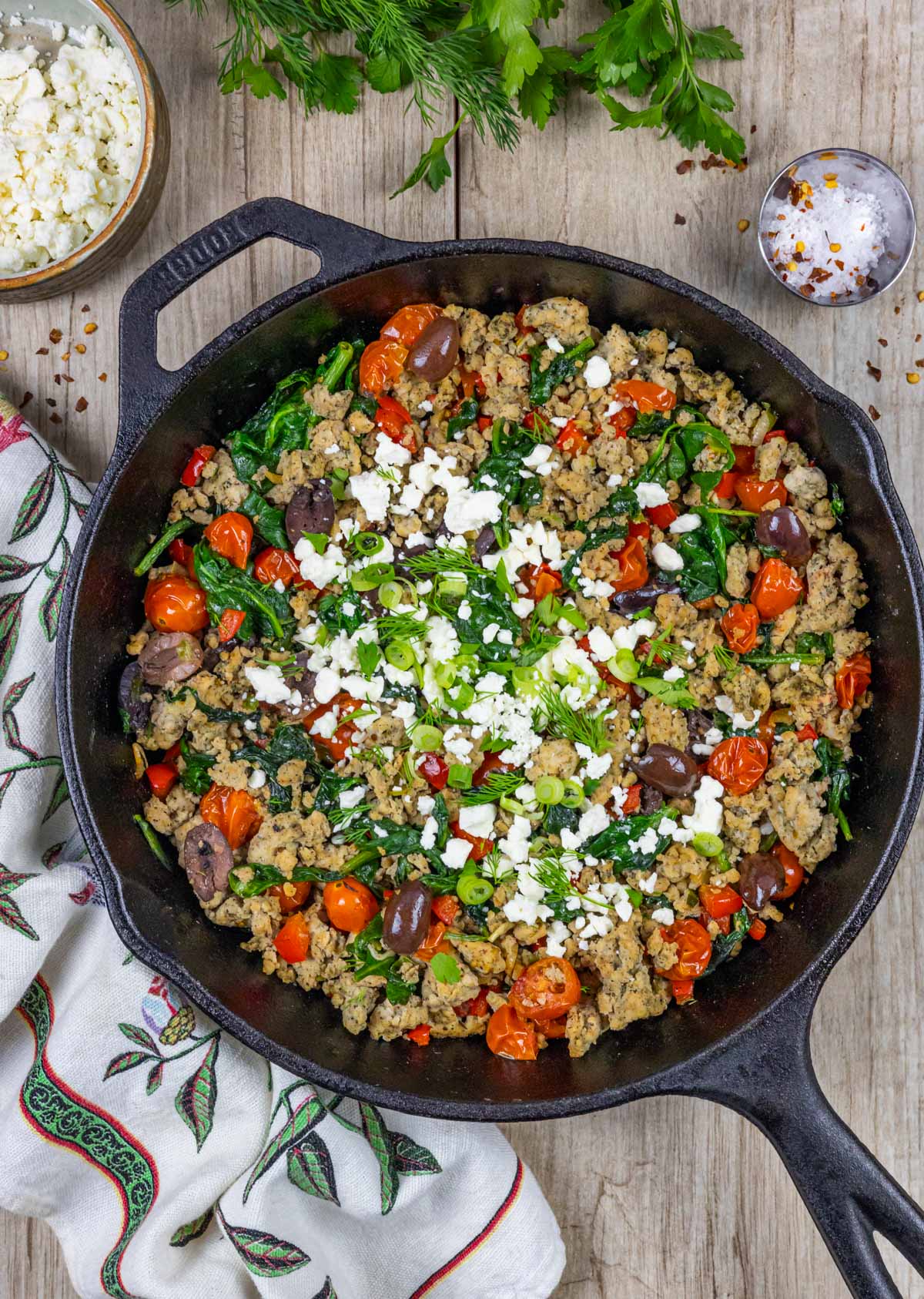 Ground chicken stir fry in a cast iron skillet garnished with dill, green onion and feta cheese.