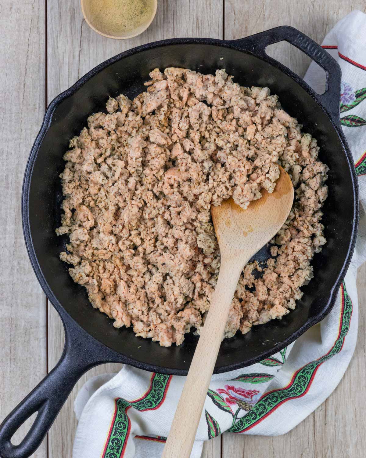 Cast iron skillet with cooked ground chicken, with a wooden spoon in the pan.