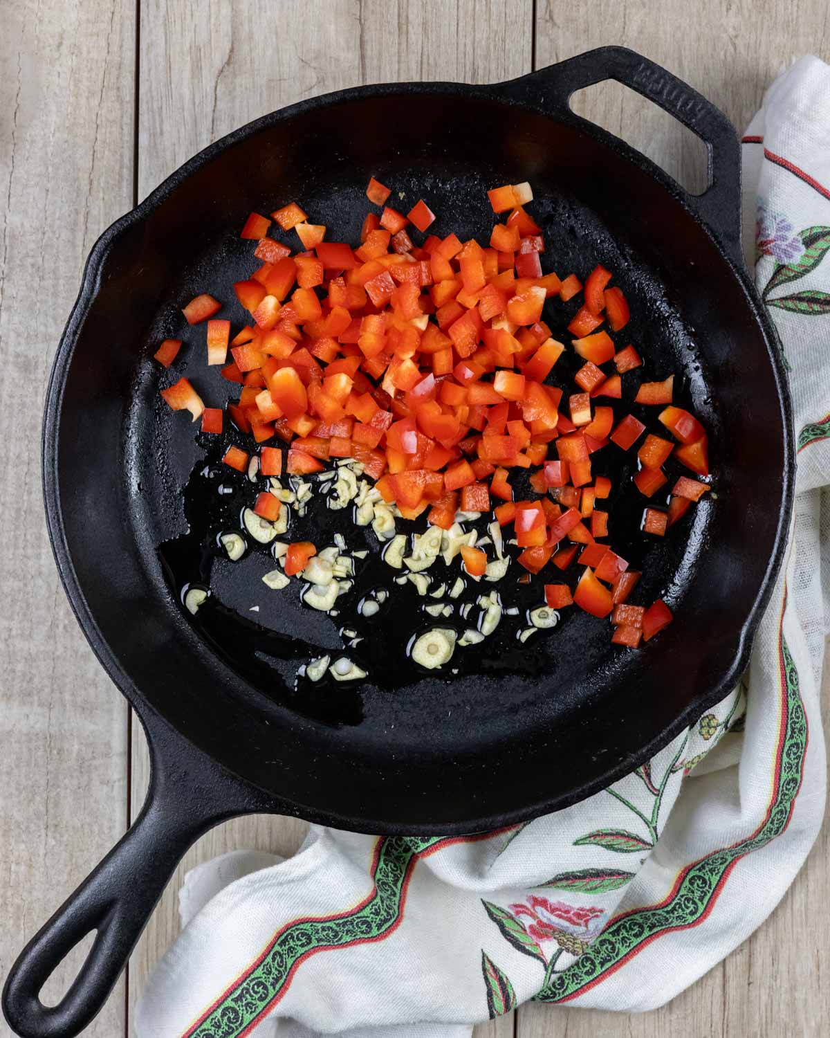 Cast iron skillet with chopped peppers, garlic and oil, ready to sauté.