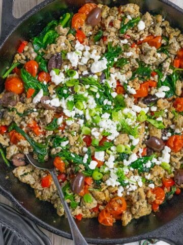 Mediterranean ground chicken stir fry served in a cast iron skillet with a spoon ready to dish up.