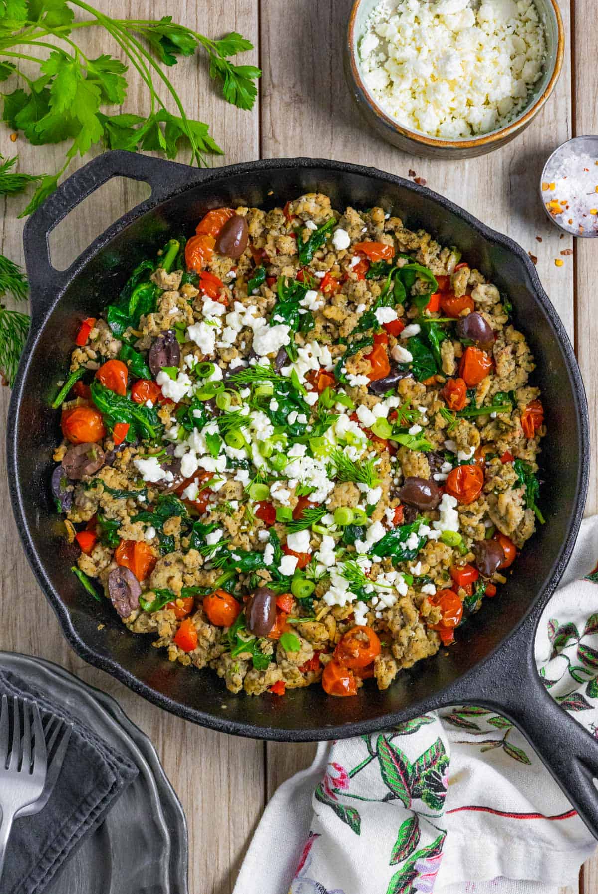 Cast iron skillet serving finished ground chicken greek stir fry topped with feta cheese, fresh dill, and chopped green onion.