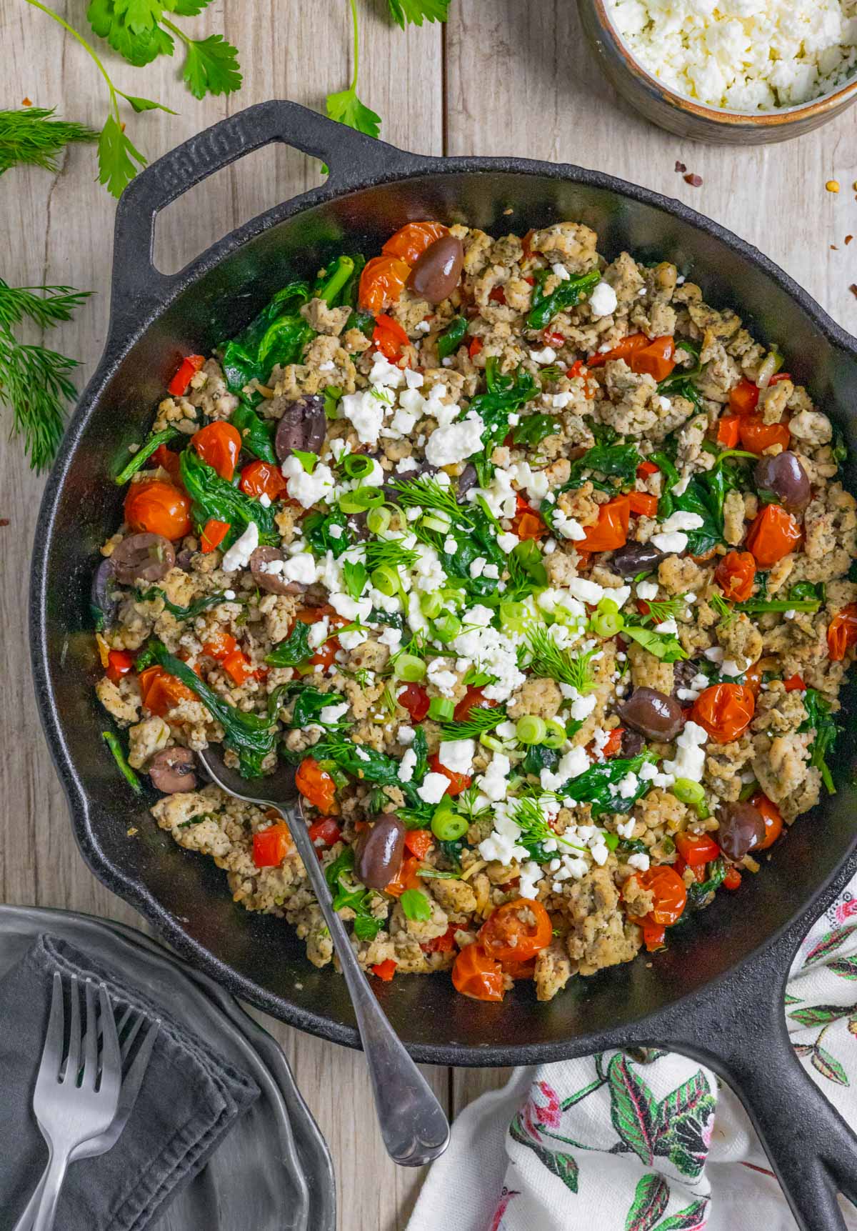 Mediterranean stir fry with ground chicken in a cast iron pan with a spoon ready to serve.