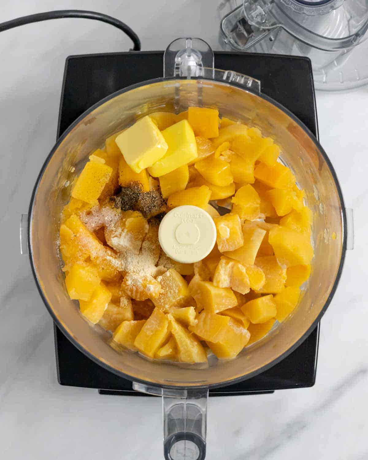 Butter and seasonings added to a food processor bowl containing cooked chunks of rutabaga ready to blend.