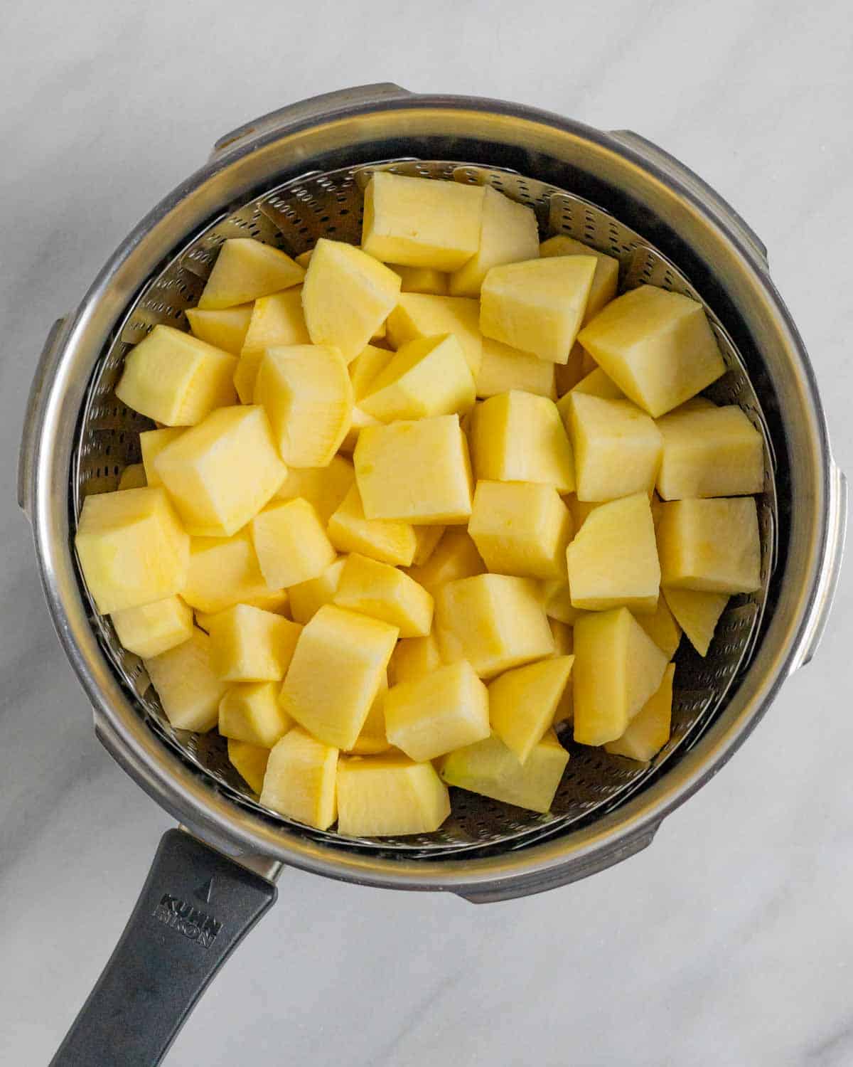 Cooked chunks of rutabaga in a steamer basket in a pressure cooker.