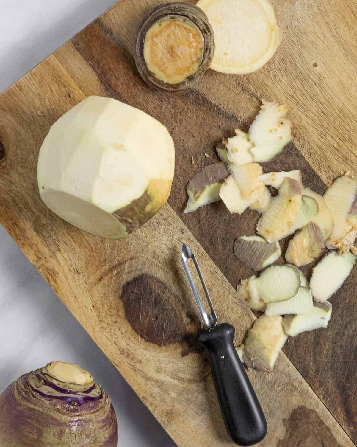 Whole rutabaga on a wood board, partly peeled with a veggie peeler.