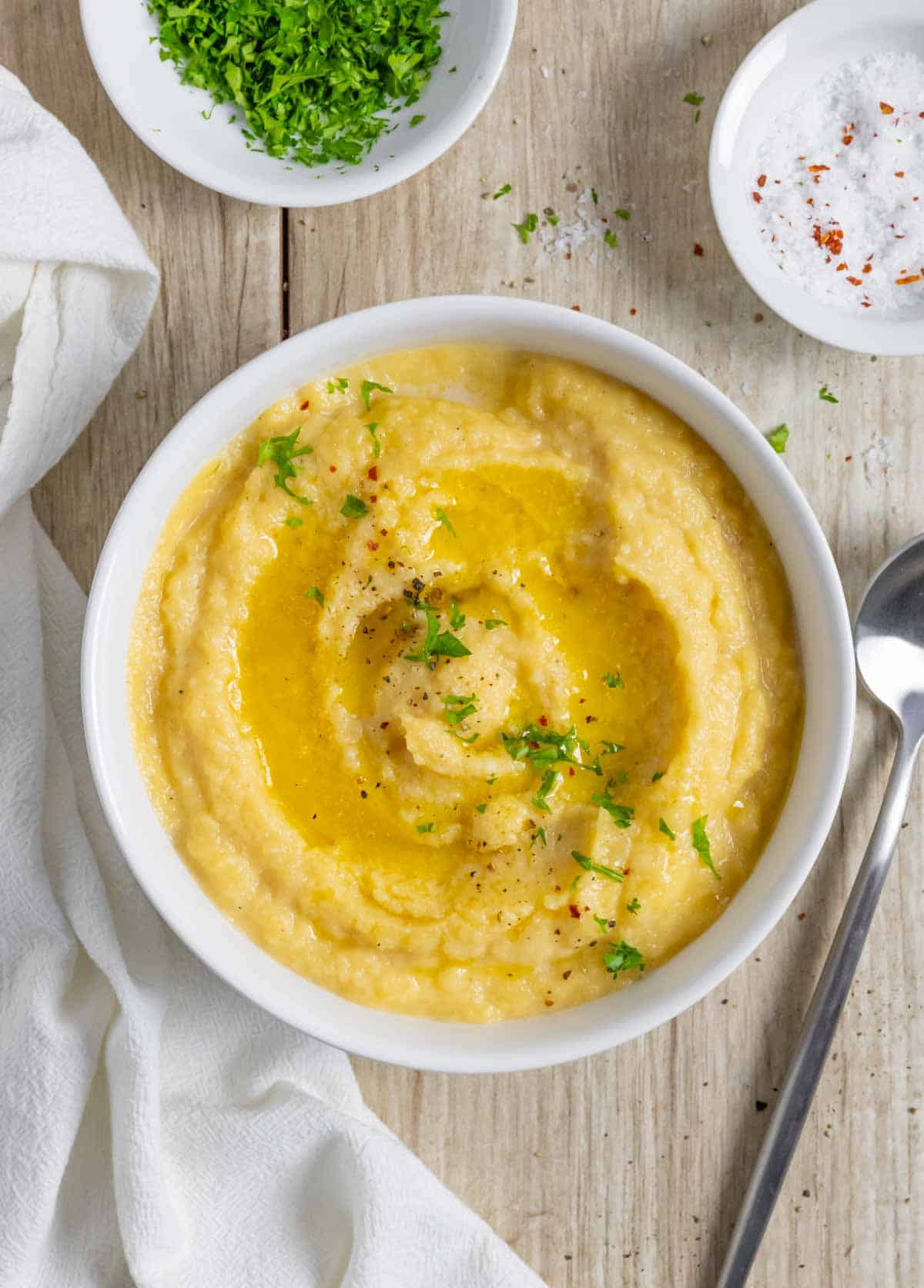 Bowl of mashed rutabaga on a board sprinkled with herbs on a wood board with a spoon.