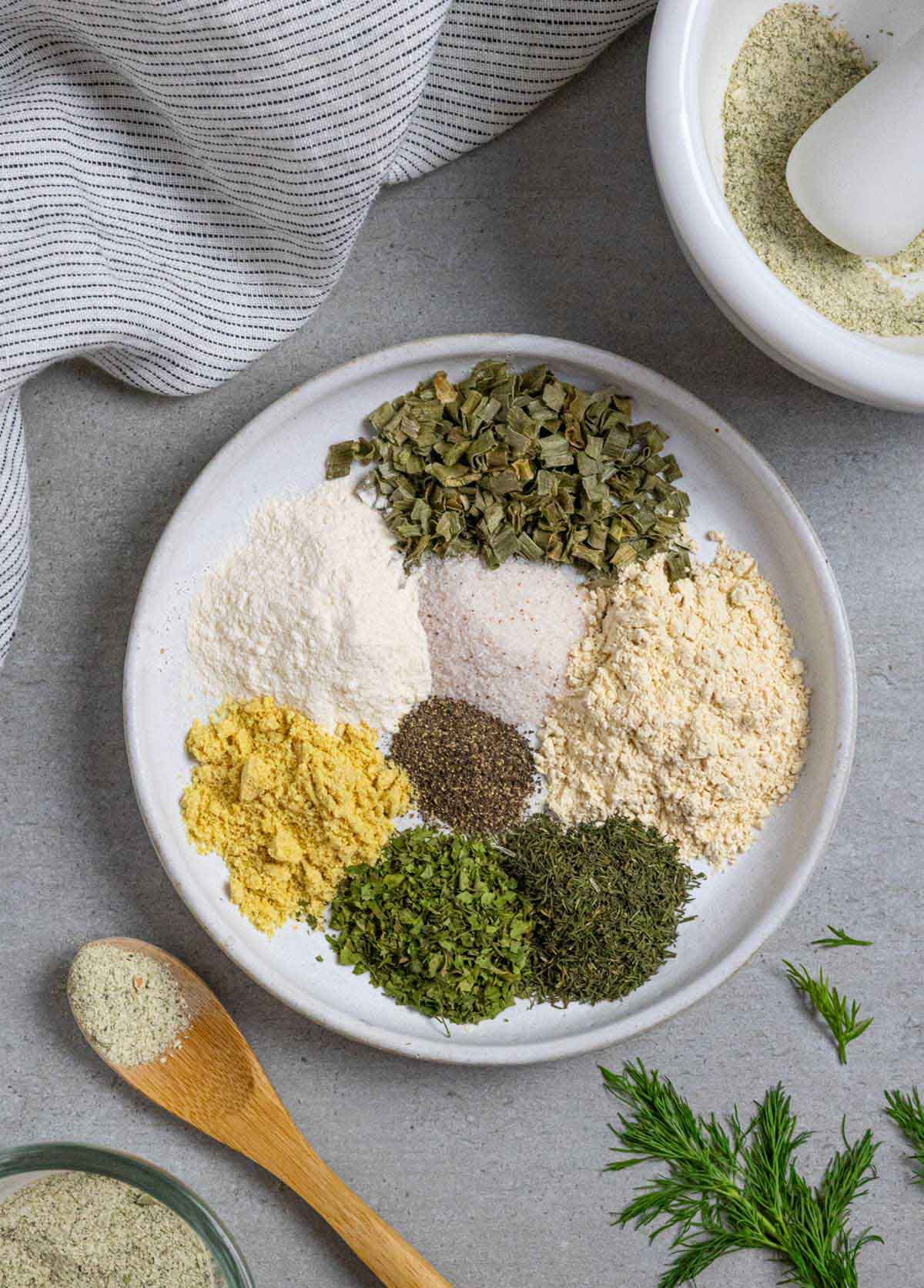 Small piles of Ingredients for ranch seasoning on a white plate with a wood spoon next to it.