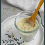 Homemade ranch seasoning in a glass jar with a wood spoon in it on a white plate.