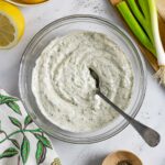 Low-fodmap ranch dressing in a clear glass bowl with a spoon in it and veggies next to it.