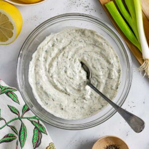 Low-fodmap ranch dressing in a clear glass bowl with a spoon in it and veggies next to it.