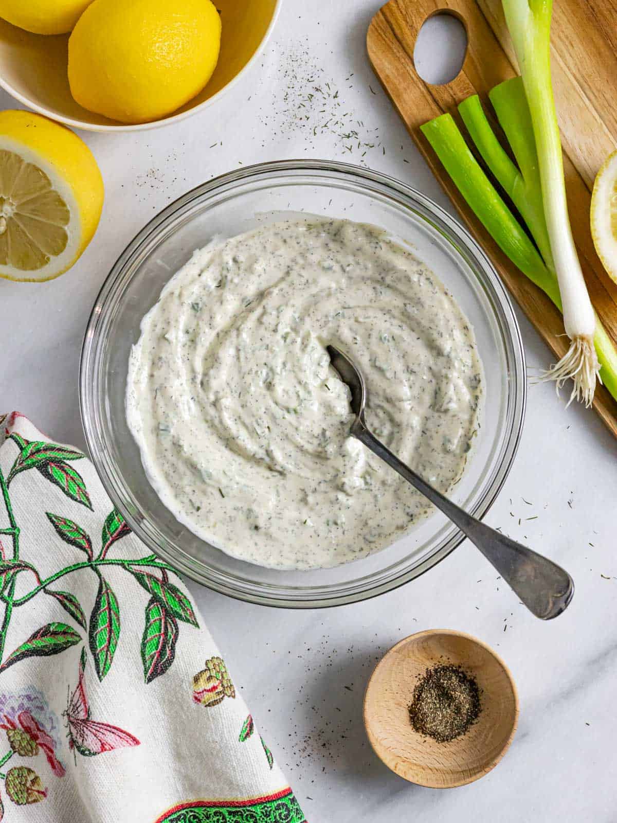Bowl of rich ranch dressing and dip with a spoon on a marble board next to a decorative towel.