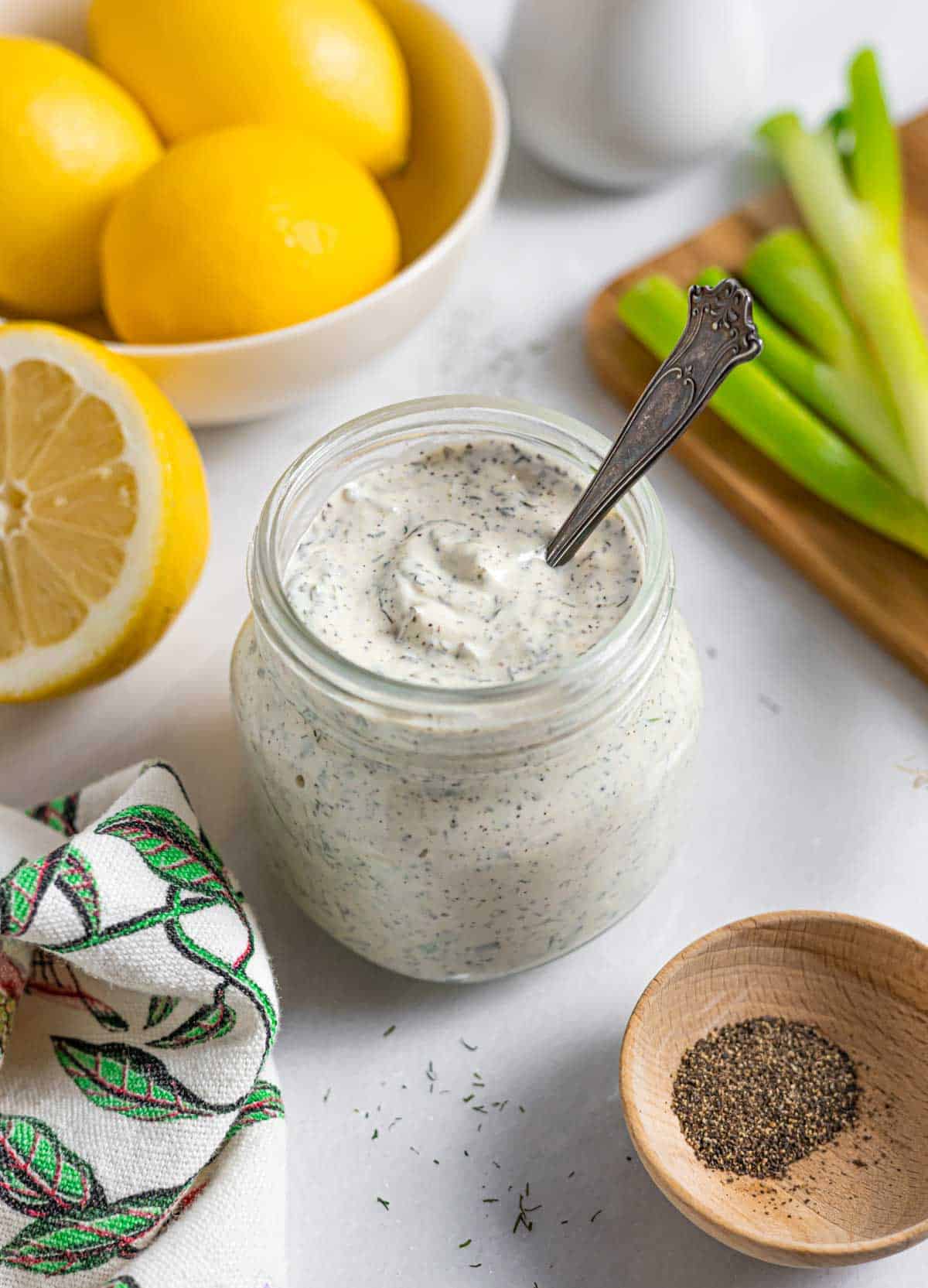 Jar of low-fodmap ranch dressing with a spoon in it on a board with a bowl of lemons and green onions.