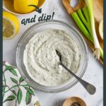Bowl of rich ranch dressing and dip with a spoon on a marble board next to a decorative towel.