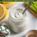 Jar of low-fodmap ranch dressing with a spoon in it on a board with a bowl of lemons and green onions.