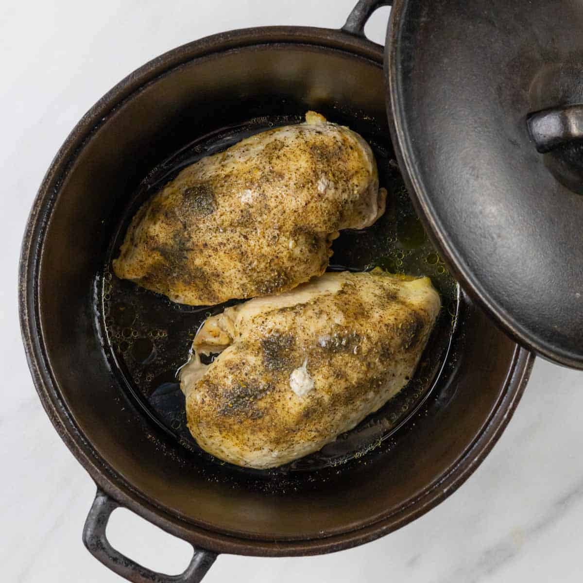 Seasoned and roasted chicken breasts baked in a cast iron pot with the lid positioned off to the side.