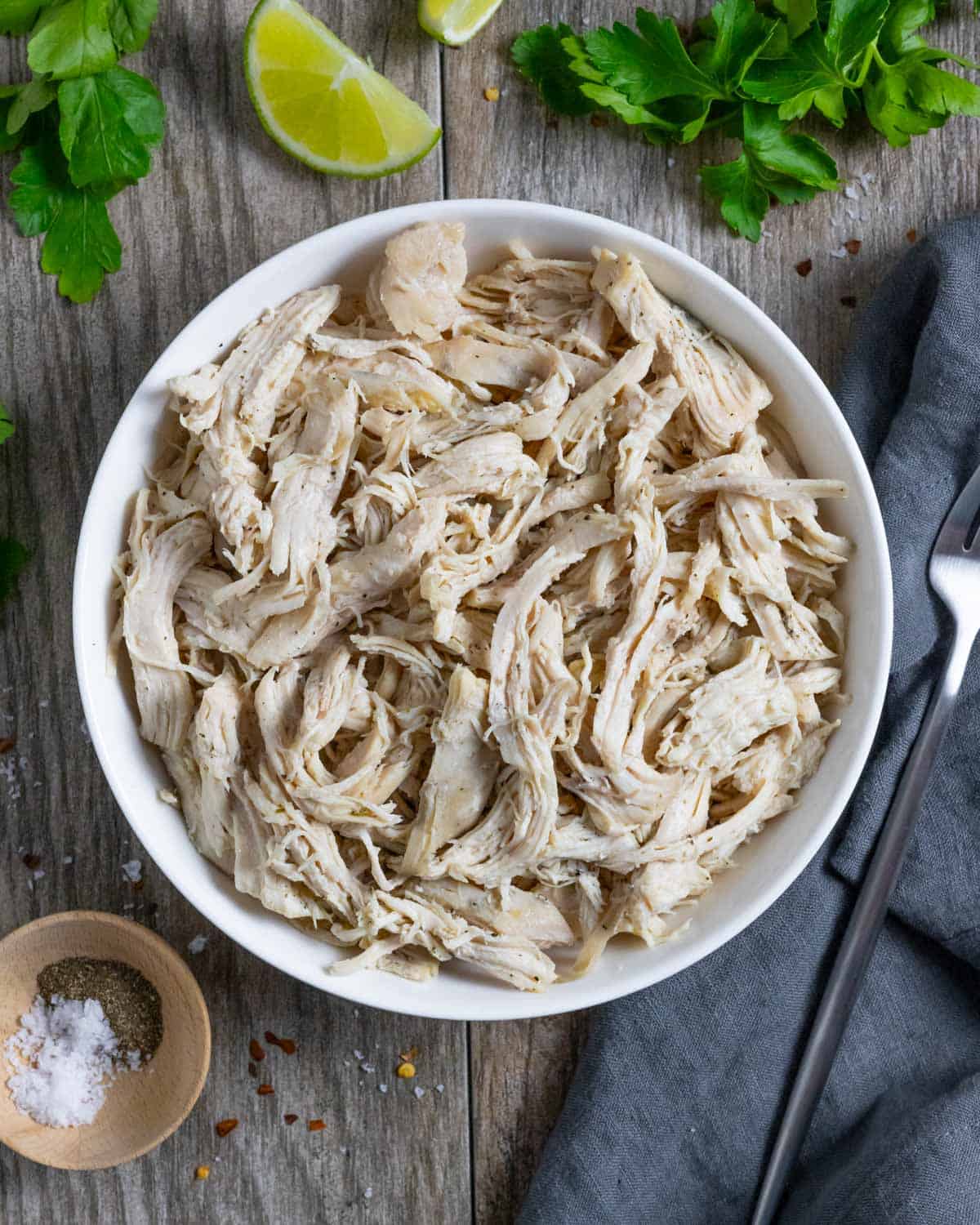 Pulled chicken breast in a white bowl with a fork and napkin on the right side.