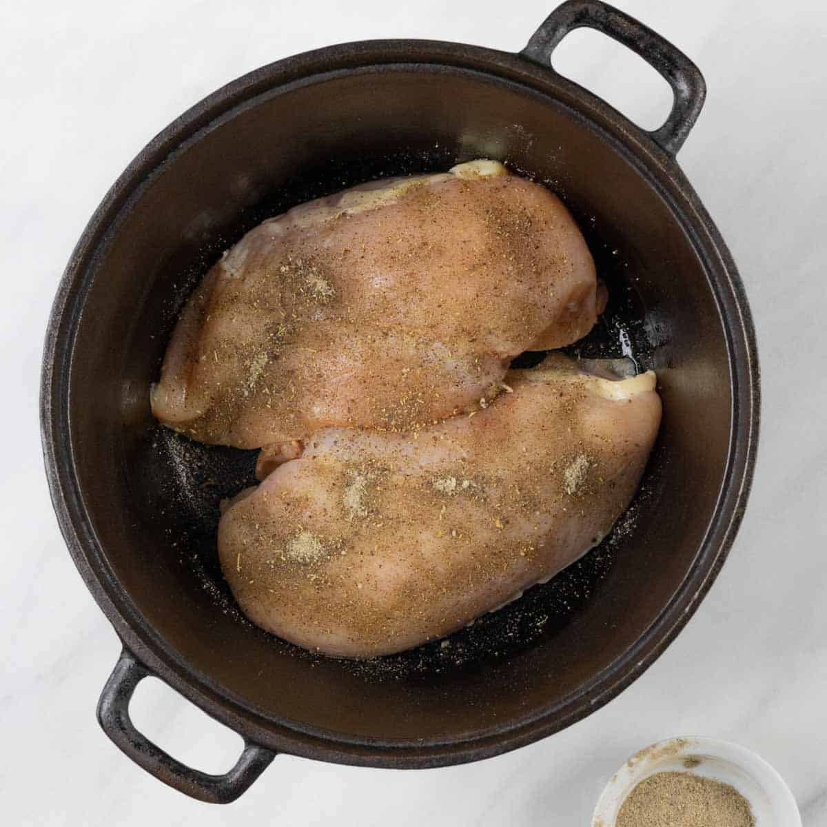 Seasoned raw chicken breasts in a cast iron pot.