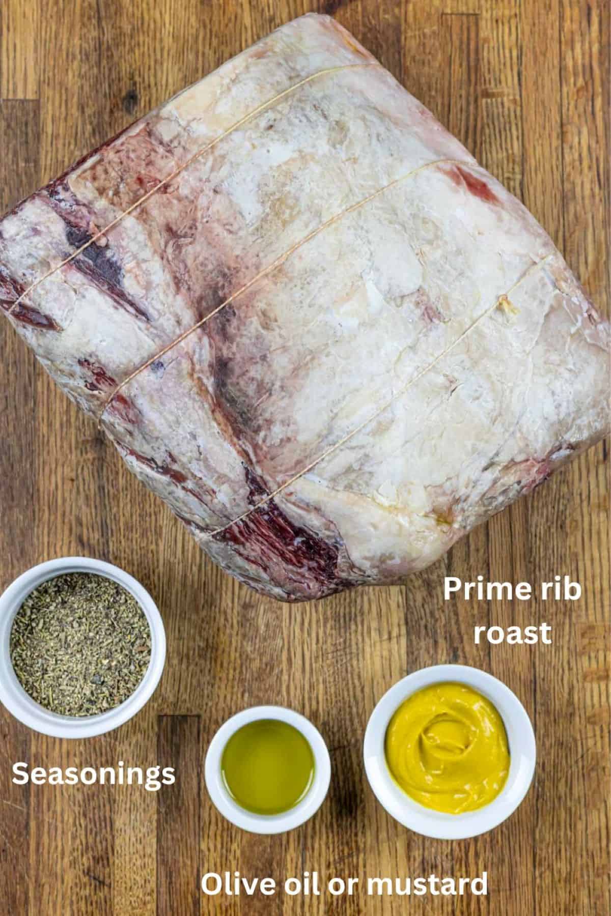 Whole tied roast on a cutting board with bowls of seasonings, olive oil and mustard