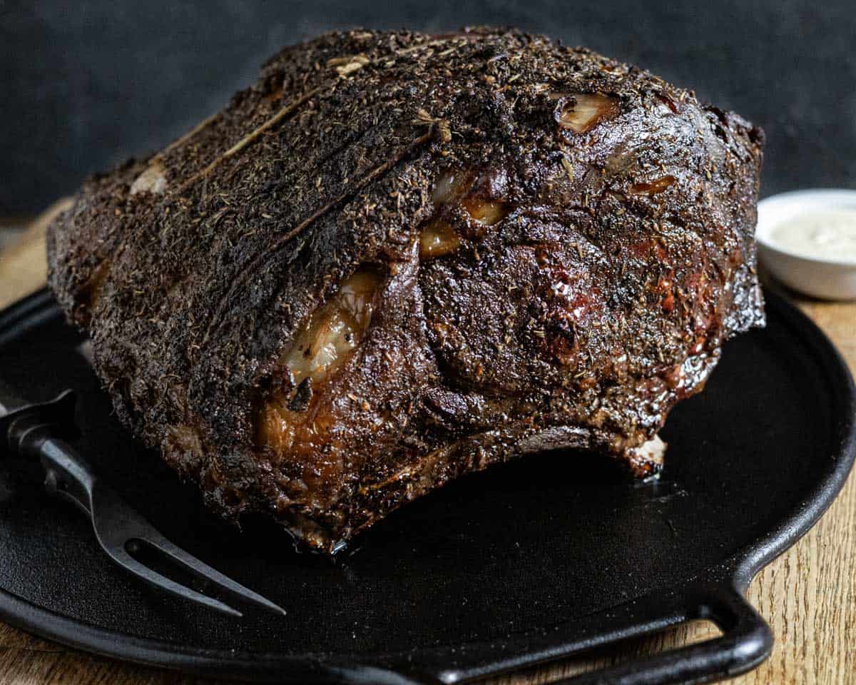 Cooked prime rib roast on a cast iron platter with a serving fork.