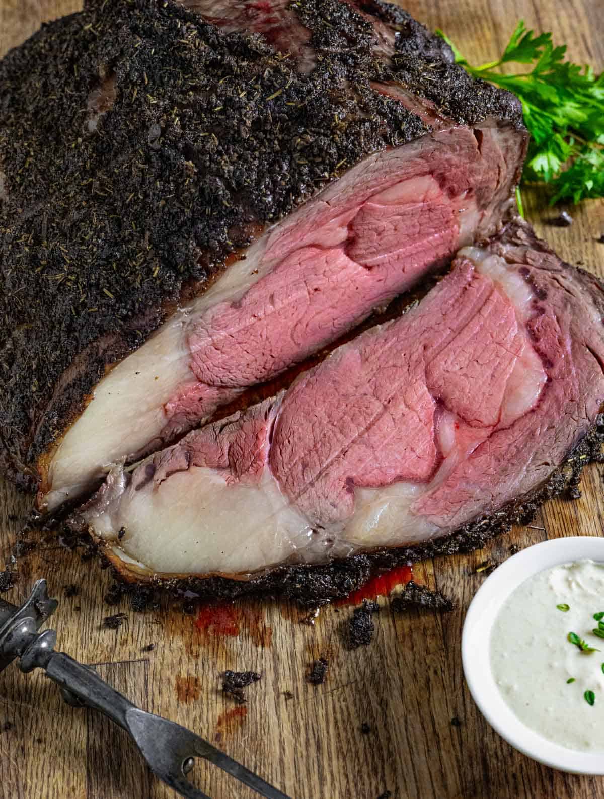 Prime rib with one sliced carved and a bowl of horseradish sauce on a cutting board